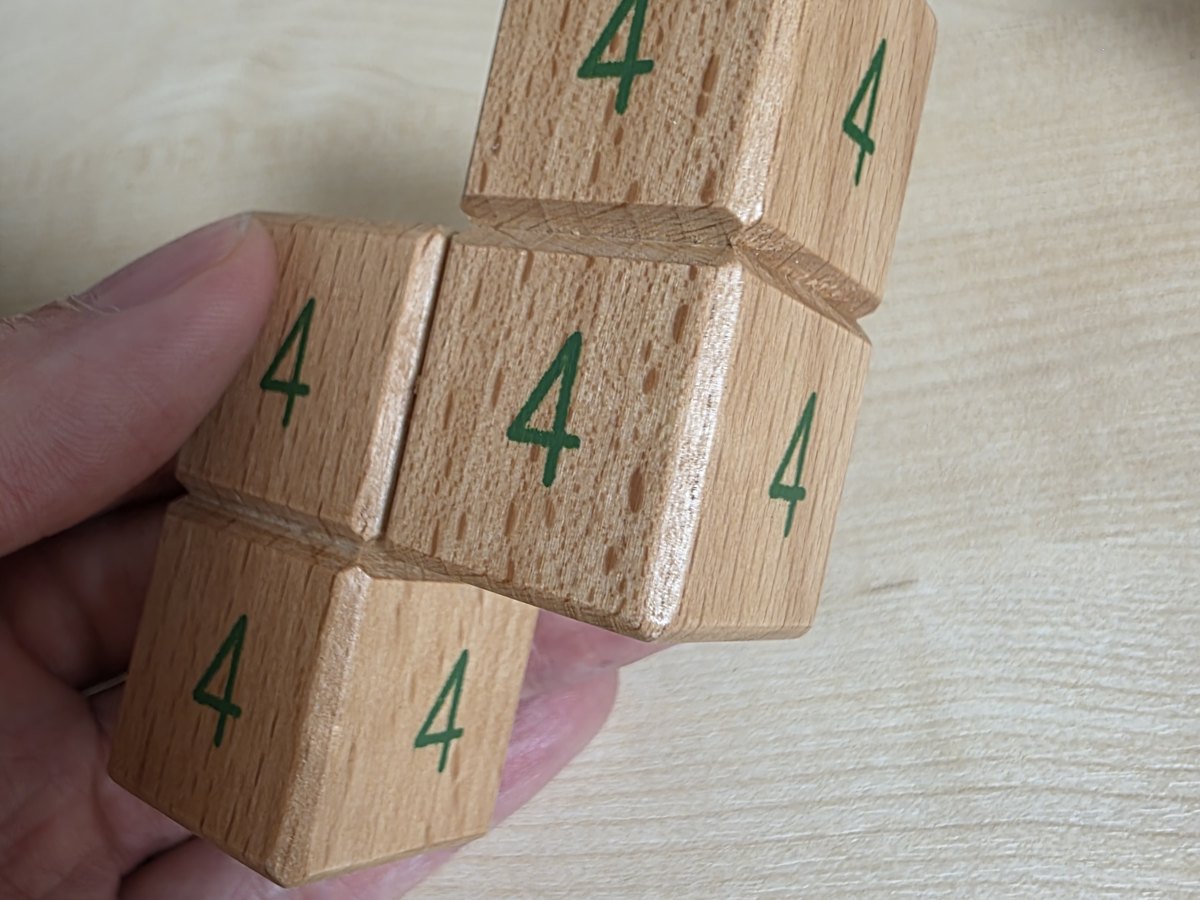 A hand holding a wooden soma piece with the number 4 painted on each face